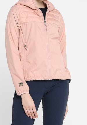 Persoon draagt een lichtroze capuchonjack met rits, elastische manchetten en zoom, gecombineerd met donkerblauwe broek.