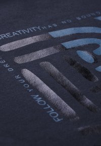 T-shirt in tessuto blu navy con grafiche testurizzate in tonalità di blu e grigio, con il testo "LA CREATIVITÀ NON HA LIMITI" e "SEGUITA I TUOI SOGNI."