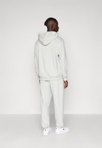 Šviesiai pilkas džemperis ir atitinkamos kelnių kelnės, pagamintos iš minkštos medžiagos, su gobtuvu ir elastingais rankogaliais, suderintos su baltais sportbačiais.