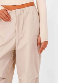 Beige, brede broek met elastische tailleband en zijzakken, van gladde stof en met een subtiel logo op de achterzak.