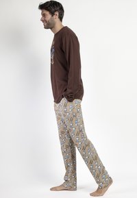 Camisa marrón de manga larga con estampado gráfico; pantalones de pijama beige con ilustraciones de Snoopy en azul y patrones triangulares. Corte casual.