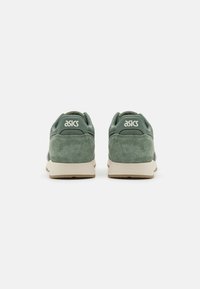 Baskets en suède vert avec des accents en maille, une semelle en caoutchouc beige clair et un logo "asics" blanc à l'arrière. Design athlétique classique.