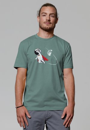 Groene katoenen T-shirt met een cartoonfiguur in een ruimtepak en een rode cape, tegen een ruimte-achtergrond met een planeet.