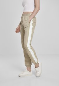 Beige joggebukser med hvite sidestiper og limegrønne detaljer, med elastisk midjebånd og smale mansjetter, sammen med hvite sneakers.