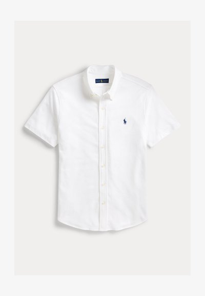 Camisa branca de mangas curtas e abotoada, confeccionada em algodão com gola apontada, apresentando um pequeno logótipo bordado em azul de polo no lado esquerdo do peito.