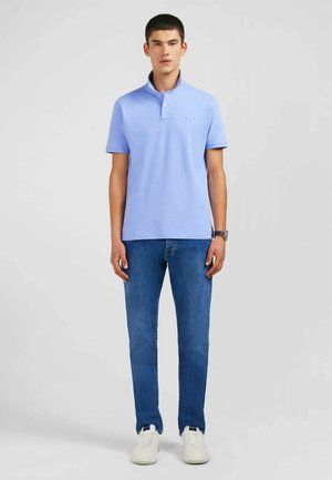 Polo shirt bleu clair avec un col et une patte de boutonnage à deux boutons, associé à un jean droit bleu foncé et des baskets blanches.