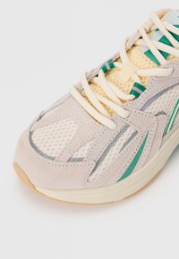 Lightweight running shoe featuring grey suede and breathable mesh upper with green accents. Rounded toe and cream laces. Durable rubber sole.