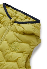 Žlutá prošívaná vesta s předním zipem, vypolstrovaným límcem a tmavě modrým lemováním kolem výstřihu, na hrudi s vyšitým logem.
