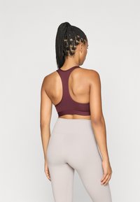 Bordeaux sportbeha met een racerback ontwerp, gemaakt van een gladde stof. Gecombineerd met hoogwaist, lichtbeige leggings.