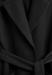 Abrigo negro hecho de un tejido texturizado con un diseño estructurado, que cuenta con un cuello con muescas y un cinturón de tela atado a la cintura.