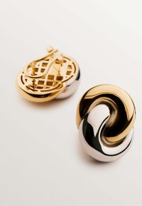 Dos broches decorativos: uno en tono dorado con un diseño de rejilla; el otro presenta una mezcla trenzada de oro y plata con una superficie lisa.