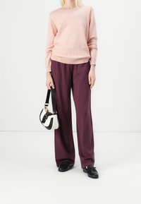 Pull en maille rose clair, coupe ample, poignets côtelés ; pantalon large violet foncé ; chaussures noires ; petit sac à main noir et blanc.