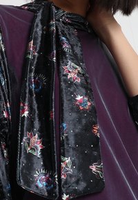 Schwarzer Samt-Schal mit mehrfarbigen Blumenmustern und Akzenten. Der Schal hat eine glatte Textur und ist am Hals gebunden.