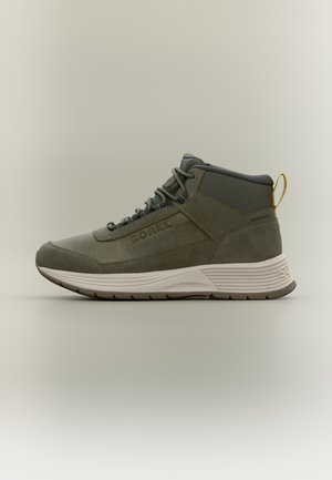 Γκρι αδιάβροχο sneaker Sorel ψηλού τύπου με κορδόνια, επενδεδυμένη λευκή σόλα και κίτρινο λουράκι στο πίσω μέρος σε ουδέτερο φόντο.