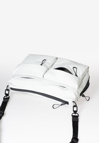 Borsa strutturata bianca con due scomparti imbottiti, zip nere e tracolla regolabile. Caratterizzata da anelli per la chiusura e texture sulla superficie.