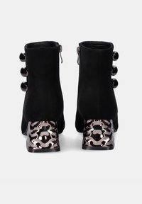 Botas de tobillo de ante negro con un exclusivo tacón metálico con corte y acentos de botones redondeados. Las cremalleras laterales facilitan su uso.