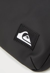 Black waterproof bag with a textured finish. Features a rectangular logo patch with a white emblem on a black background.