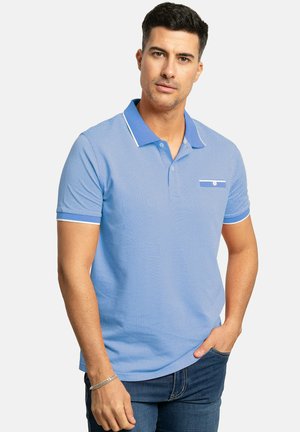 Camisa polo azul claro con tejido texturizado, cuello azul sólido en contraste y ribetes blancos. Presenta un bolsillo en el pecho con un detalle de botón.