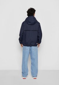 Navy blue, lightweight hooded jacket with a relaxed fit and elastic cuffs. Features a back flap and subtle logo detail at the hem.