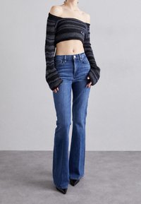 Mustat ja harmaat raidalliset olkapäistä paljastava neulecrop-toppi, jossa on leveät hihat, yhdistettynä korkeavyötäröisiin sinisiin leveneviin farkkuihin ja teräväkärkisiin mustiin korkokenkiin.