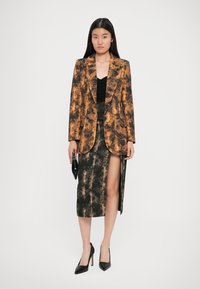 Blazer im orange-schwarzen Muster, taillierte Passform; kombiniert mit einem schwarzen Satin-Midirock mit hohem Schlitz, schwarzen Absätzen und einer Clutch.