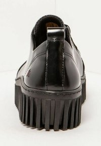 Zapatos de cuero negro con un acabado brillante, que cuentan con una suela gruesa y estriada, y una pestaña en el talón en forma de bucle para facilitar su uso.