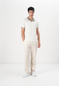 Helles Strick-Polohemd mit einem kontrastierenden Kragen, kombiniert mit hellbeigen Hosen und weißen Sneakern. Einfaches, klares Design.
