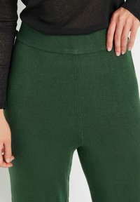 Groene gebreide broek met een geribde tailleband, met een zachte textuur en een ontspannen pasvorm. De stof heeft een uniforme kleur en een gladde afwerking.