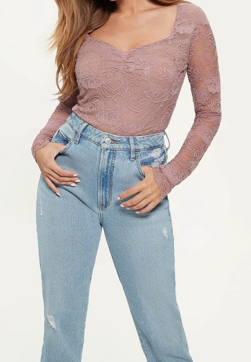 Langärmliges Spitzenoberteil in hellem Mauve mit quadratischem Ausschnitt und floralen Muster, kombiniert mit hoch geschnittenen, lässigen hellblauen Jeans.