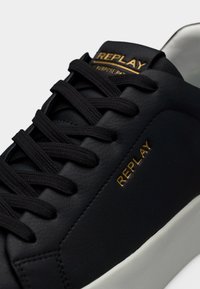 Μαύρο δερμάτινο αθλητικό παπούτσι με υφή, με χρυσό λογότυπο "REPLAY", μαύρα κορδόνια και λευκή λαστιχένια σόλα.