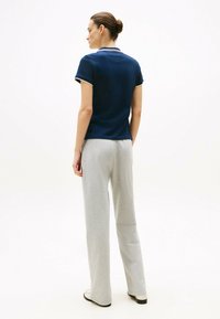Granatowa koszulka polo z krótkim rękawem i białymi detalami, w zestawieniu z jasnoszarymi, luźnymi spodniami dresowymi. Materiał wydaje się gładki i codzienny.
