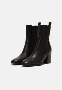 Botas de cuero negras hasta el tobillo con punta afilada, paneles laterales elásticos y un tacón grueso. Textura suave con un diseño minimalista.