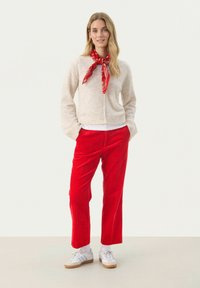 Bež kardigan, rdeč šal, rdeče kord pants in bele superge. Kardigan ima preprost dizajn z gumbi; hlače so ravno krojene.