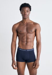Námornícké modré boxerky s páskou s logom GANT; priliehavý strih, hladká tkanina, žiadne viditeľné vzory ani ozdoby. Model stojí vzpriamene.