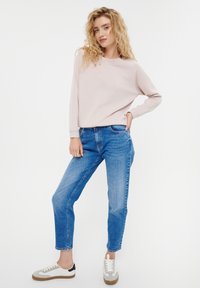 Felpa rosa chiaro con maniche lunghe, abbinata a jeans blu a vita alta e sneakers grigie con accenti bianchi e neri.