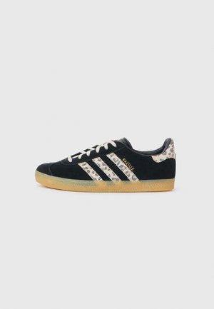 Baskets Adidas Gazelle noires avec des bandes et un talon imprimé léopard, lacets blancs et semelle en gomme, vues de côté gauche sur fond blanc.