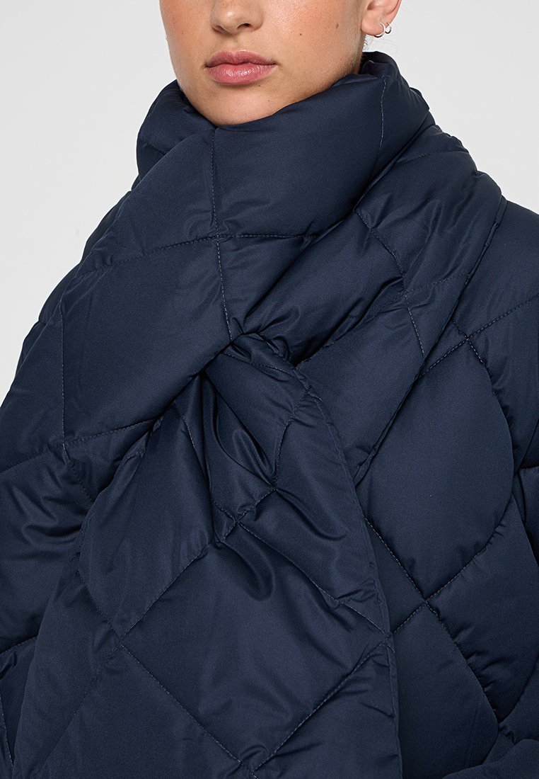 Granatowa puchowa kurtka z diamentowym przeszyciem, z wysokim kołnierzem i gładką, błyszczącą fakturą. Idealna dla zapewnienia ciepła i wygody.