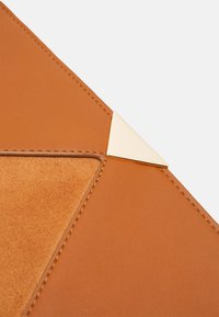 Bolso de mano de cuero marrón con superficie texturizada, diseño geométrico y acento de metal dorado en la esquina.