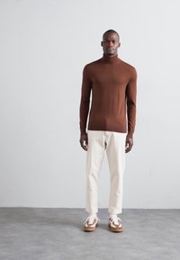 Rjav dolg rokav turtleneck, ozek kroj, v kombinaciji s kremnimi hlačami in večbarvnimi supergami. Preprost dizajn, gladka tekstura.