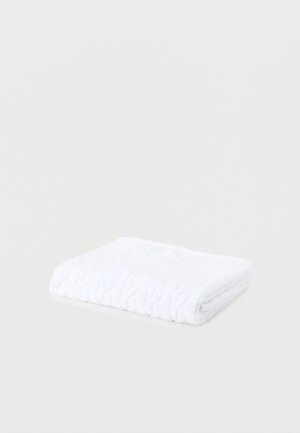 Διπλωμένη λευκή πλεκτή κουβέρτα με πλεγμένο σχέδιο σε απλό ανοιχτό γκρι φόντο.