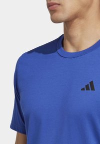 T-shirt de sport bleu royal avec un col rond et des manches courtes. Présente un logo noir à trois rayures sur la zone gauche de la poitrine.