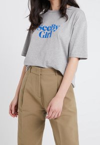 Camiseta gris de manga corta con el texto azul "SeeBy Girl". Combinada con pantalones de pierna ancha de talle alto en color caqui y textura. Diseño minimalista.