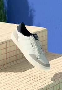 Witte sneakers met grijze en marineblauwe accenten, met een leren bovenkant, gestructureerde suede details en een rubberen zool. Merkwaarde op de tong.
