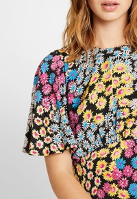 Nahaufnahme einer Frau in einem schwarzen Kleid mit bunten Blumenmustern in Pink, Blau, Gelb und Weiß.