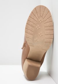 Scarpa in pelle marrone con suola testurizzata; presenta un tacco basso impilato e dettagli di cucitura. La suola ha un design grip a motivo.