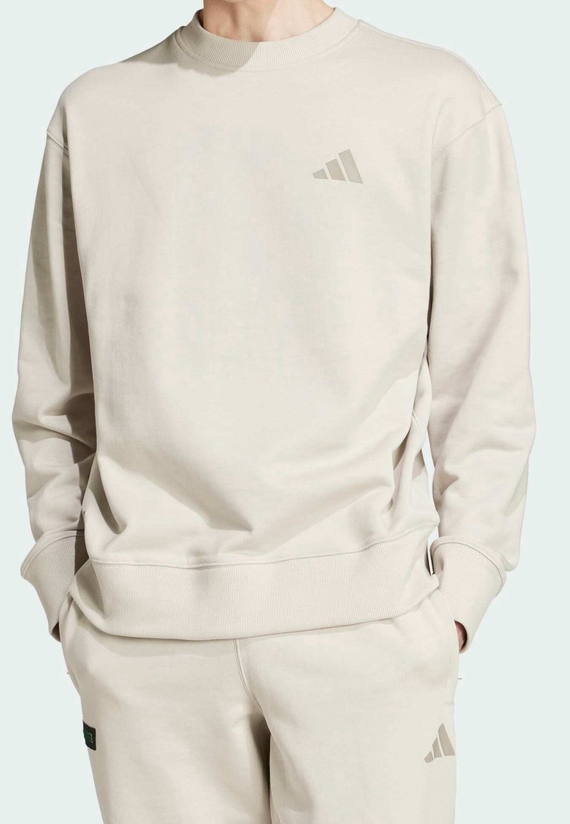 Béžová mikina s vroubkovaným výstřihem a manžetami. Obsahuje jemné logo na hrudi. Vyrobena z měkkého materiálu s volným střihem.