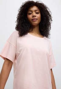 Ροζ βαμβακερό t-shirt με στρογγυλή λαιμόκοψη και κοντά, φαρδιά μανίκια. Φέρει εκτύπωση "slow morning Club" σε λευκό χρώμα. Μαλακή υφή και άνετη γραμμή.