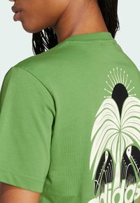 Green cotton t-shirt featuring a black and white tropical design with palm leaves and two birds. Short sleeves and a crew neckline.
