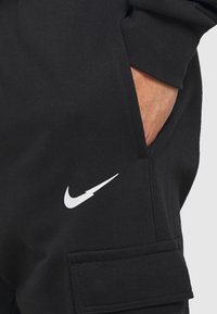 Svarta sweatpants i bomullsblandning; har en vit Nike-logotyp, sidofickor och en strukturerad yta.