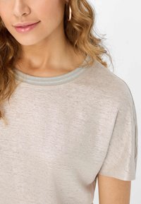 T-shirt beige chiaro con un tessuto morbido e strutturato, caratterizzata da un collo rotondo con due strisce orizzontali azzurro chiaro. Maniche corte.